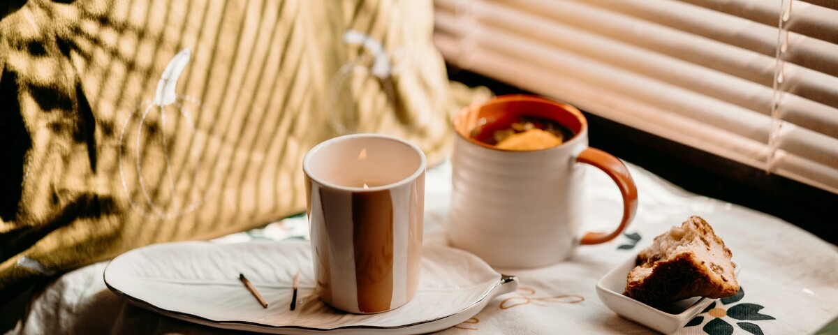 A lit candle and a mug of tea on a tray by a sunlit window