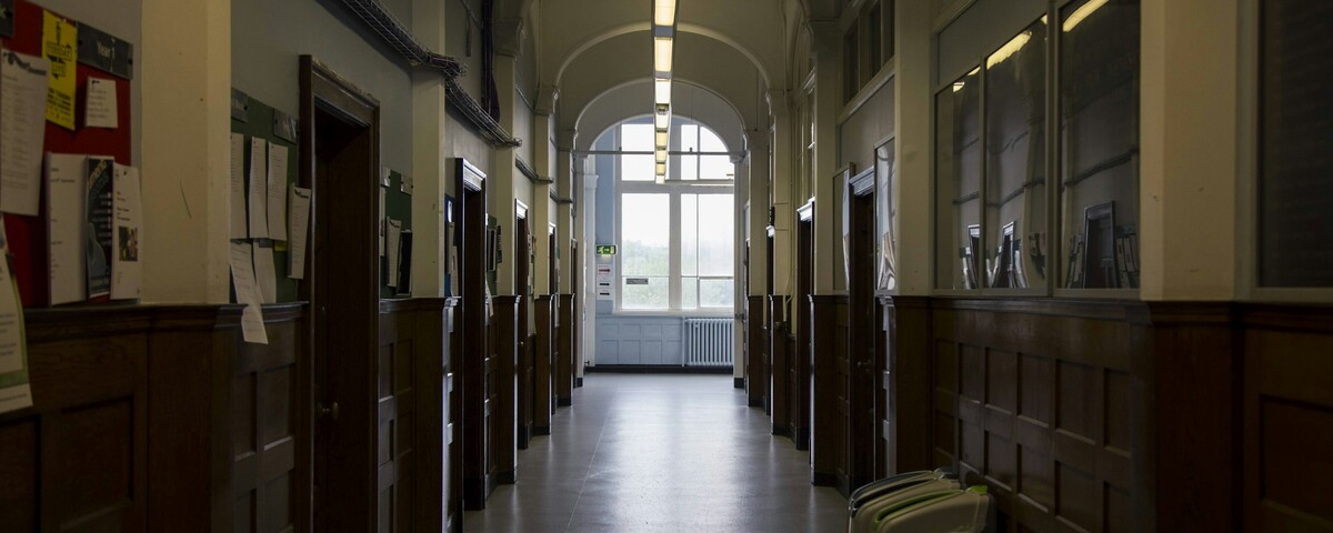 A university hall corridor with noticeboards and a suitcase left by the wall