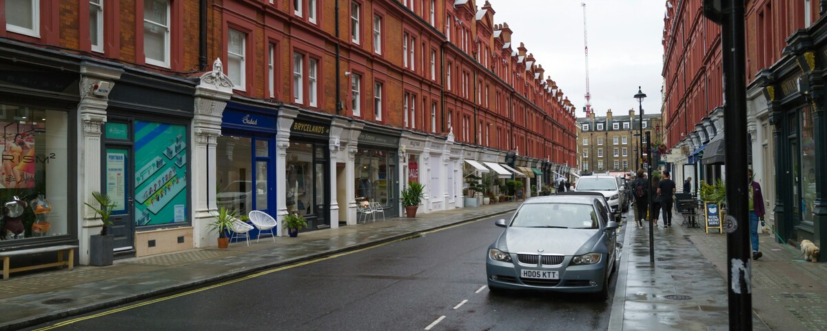 A rain-wet London street of red brick mansion blocks and small shops