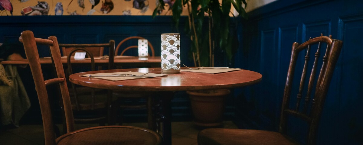 An empty round table laid with menus and a lamp, chairs pulled up around it