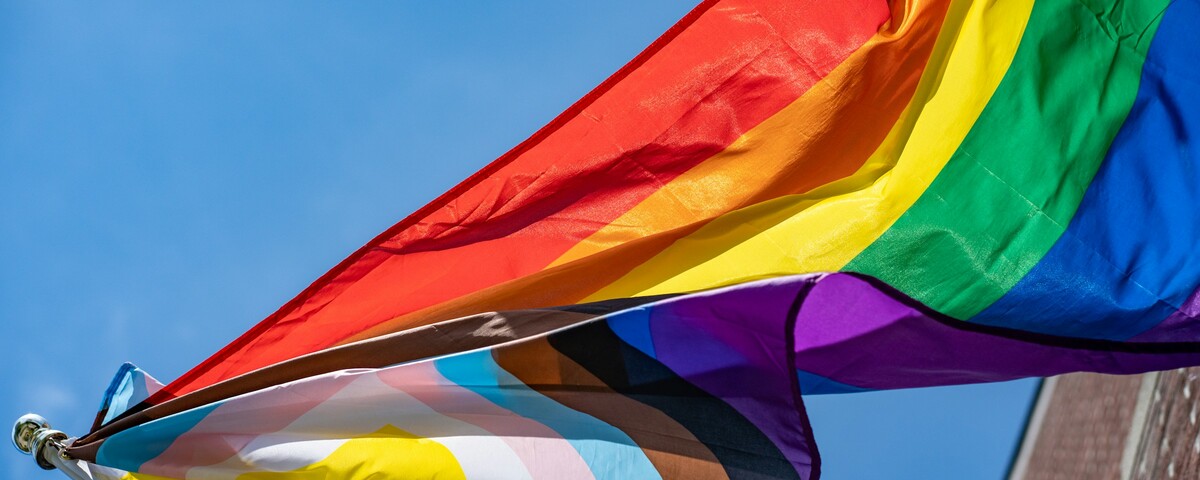 A rainbow flag lifting in the wind against a clear sky