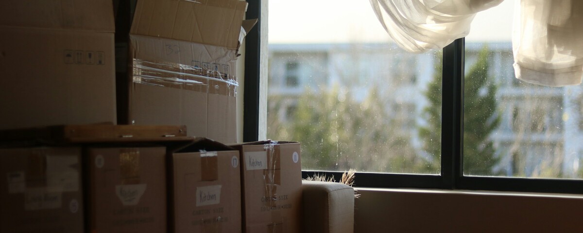 Packing boxes stacked in an empty room beside a bare window