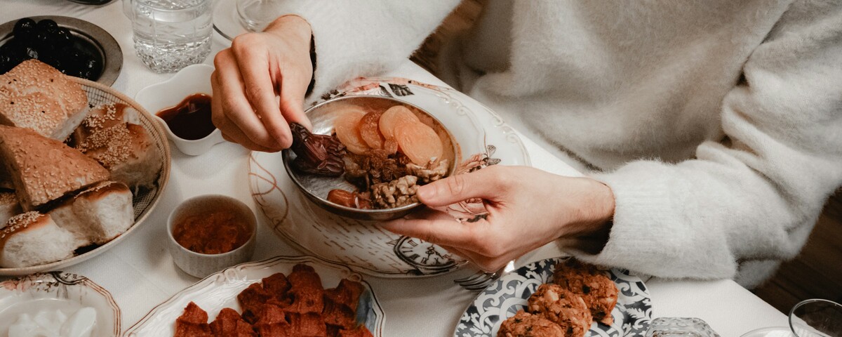 Hands reaching for dates on an iftar table laid with shared dishes